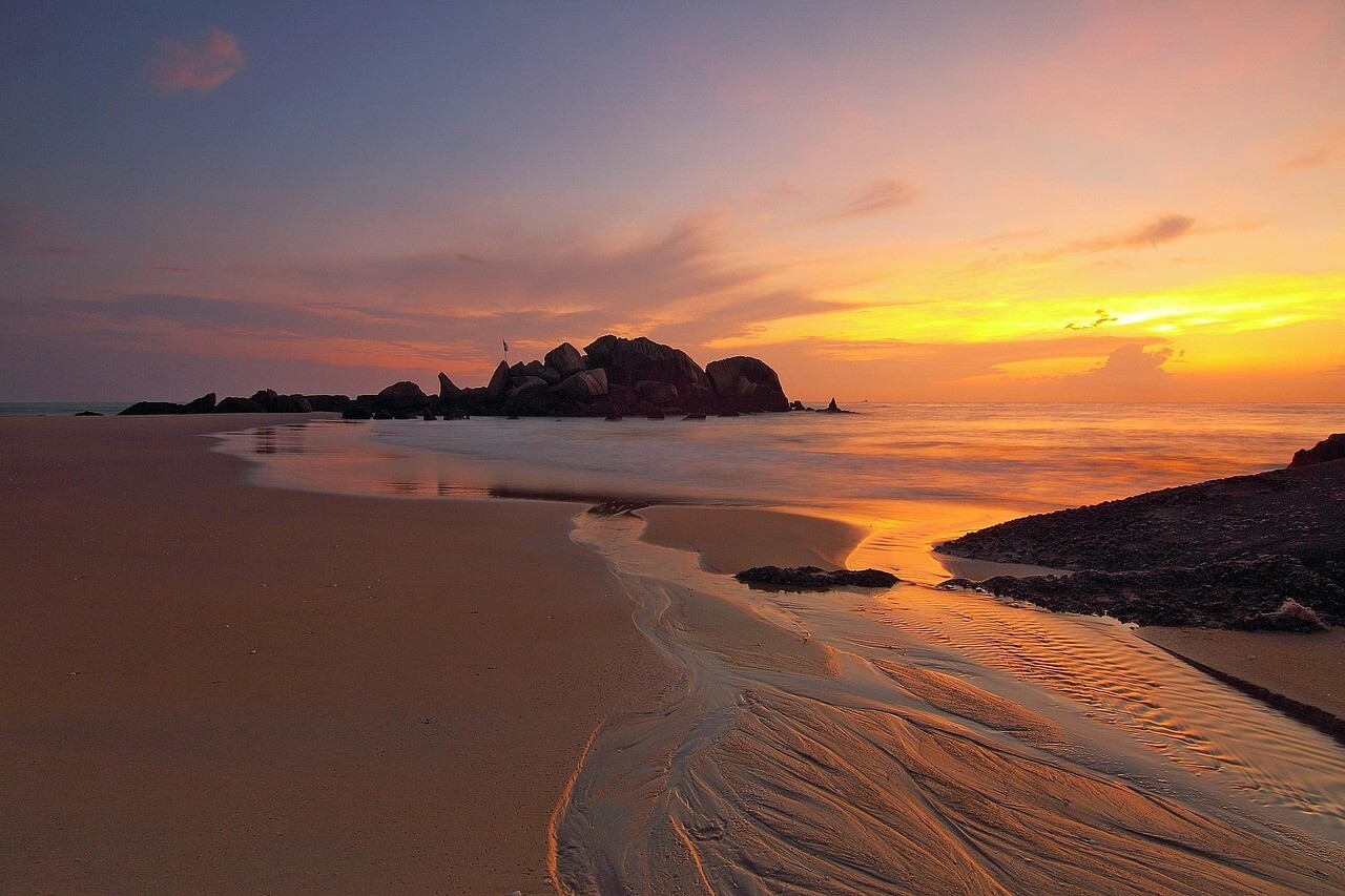 Sonnenuntergang &uuml;ber dem Meer mit Felsen &ndash; Symbol f&uuml;r Sunset-Klauseln im Investitionsschutzrecht